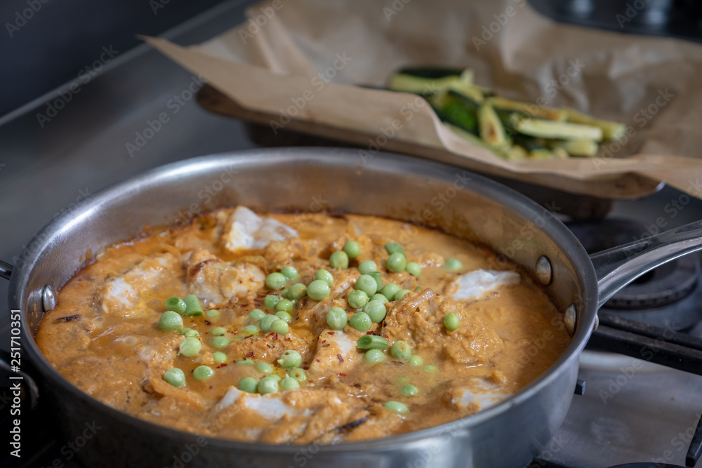 fish curry cooking in pan with baked courgettes in background fish curry cooking in pan with baked courgettes in background