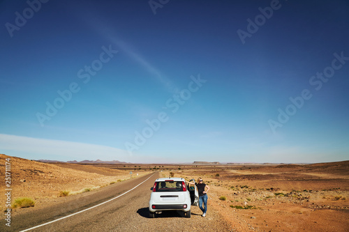 A blonde tourist girl at the car in the dessert during midday with no traffic at the road