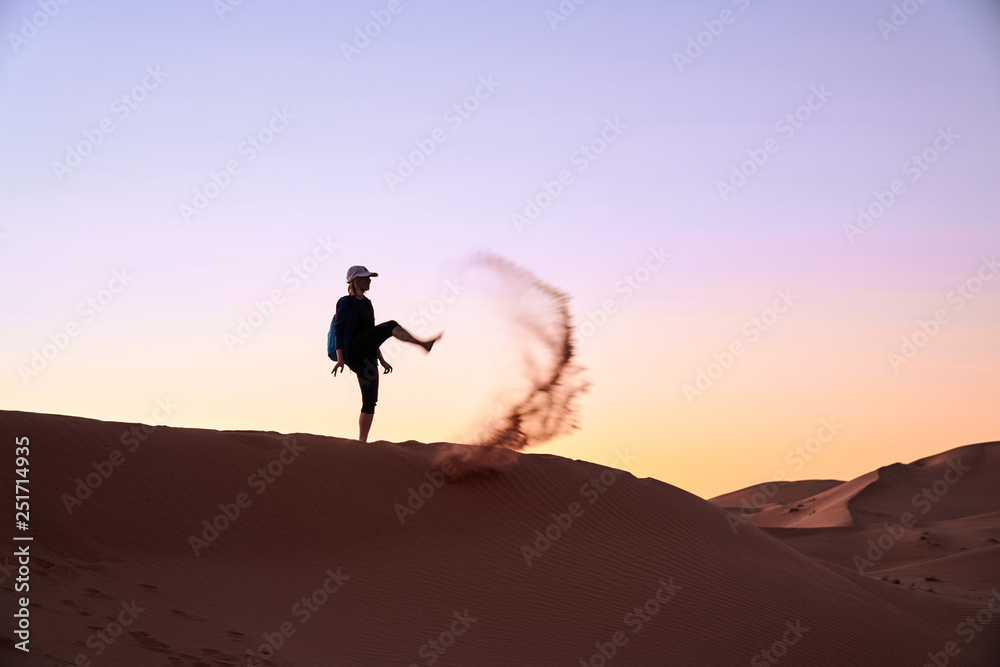 Happy tourist girl kicks into the sand on the dune in Sahara desert Morocco at the sunset