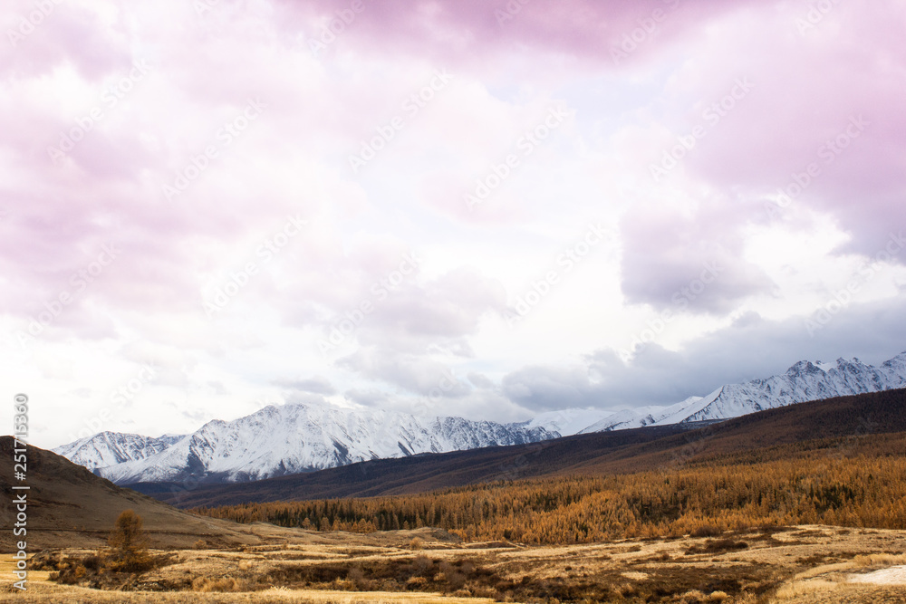 Pink clouds over mountain range. Rocks under snow on horizon. Sunset in mountain valley