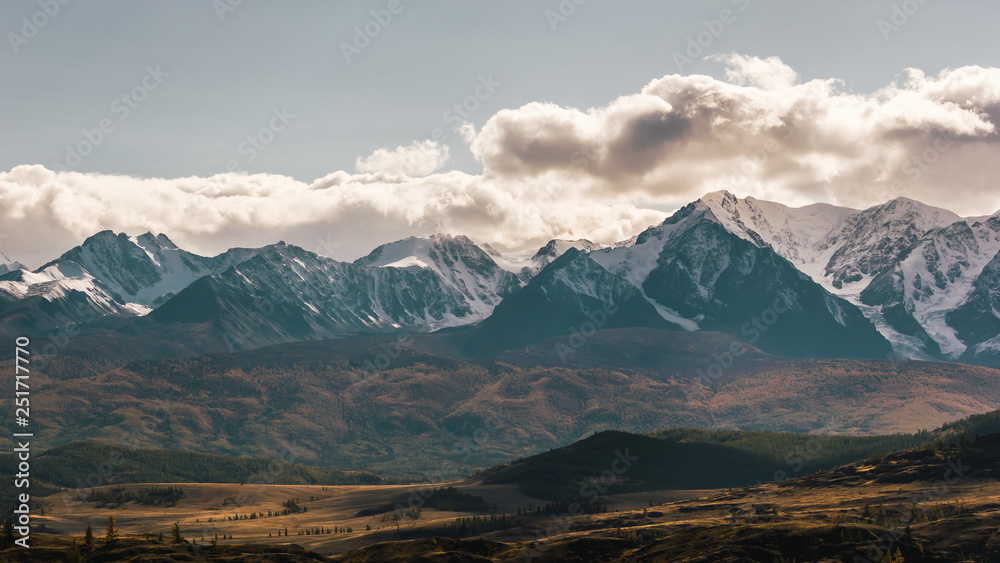 Valley with ridge of rocks on horizon. Snowy ridge of mountains under autumn sky