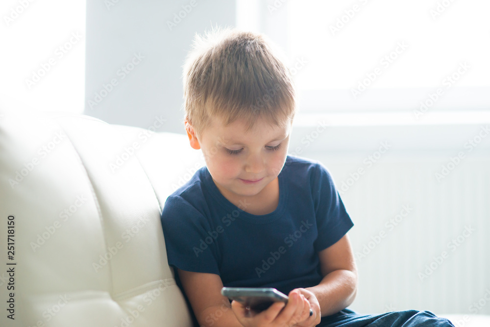 Portrait of happy boy playing with a smartphone. Kid with a mobile phone at home. Entertainment technology, futuristic gadgets, internet and generation Z concept. Portrait of happy boy playing with a smartphone. Kid with a mobile phone at home. Entertainment technology, futuristic gadgets, internet and generation Z concept.
