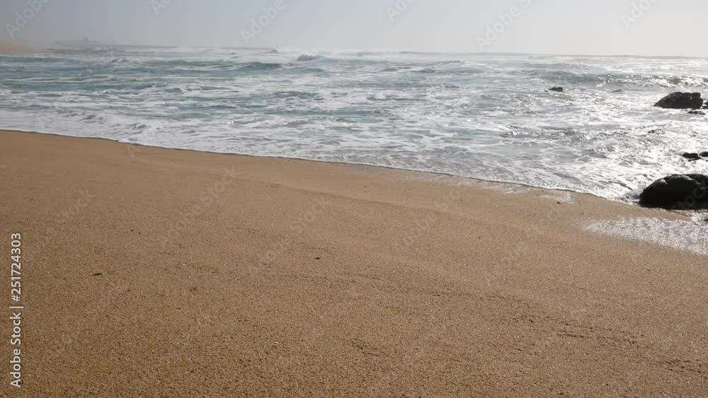 Wide angle view of white surf waves breaking on the sandy shore of the beach. Fog on the horizon on a misty day. Wide angle view of white surf waves breaking on the sandy shore of the beach. Fog on the horizon on a misty day.