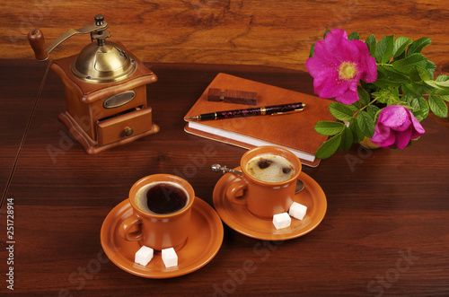 Two cups of coffee, coffee grinder, notebook, pen and rosehip flower