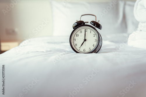 Analog Alarm Clock on Bedroom in Modern House, Retro Timer at 7.00 a.m. on White Cover Bed.