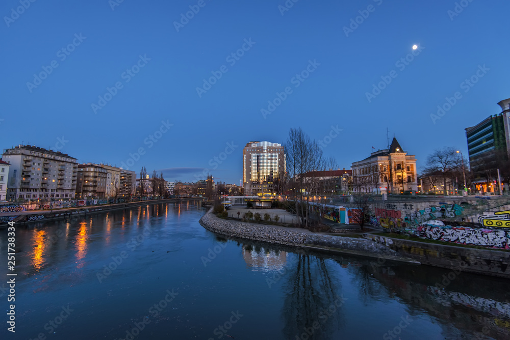Vienna, Austria - December 29, 2017. Evening view of Wien river flows through the city of Vienna with lights and buildings reflected in water. Viennese embankment with graffiti and murals at dusk.