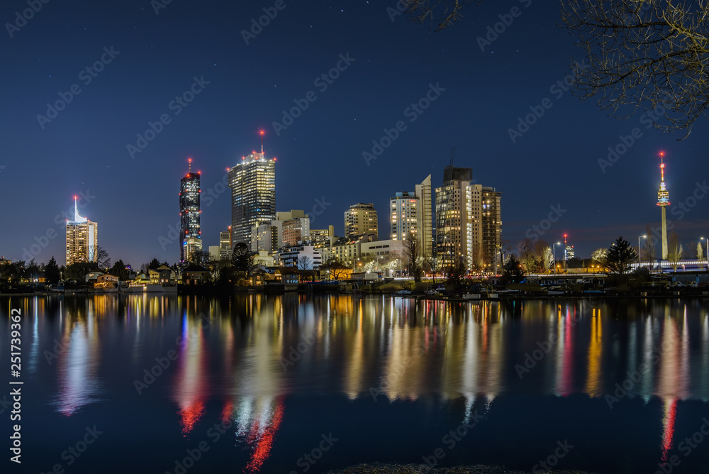 Fototapeta premium Vienna, Austria - December 29, 2017. Evening view of Donau City or Vienna DC with Andromeda Tower and modern architecture buildings reflected in water. Danube canal with illuminated business district.
