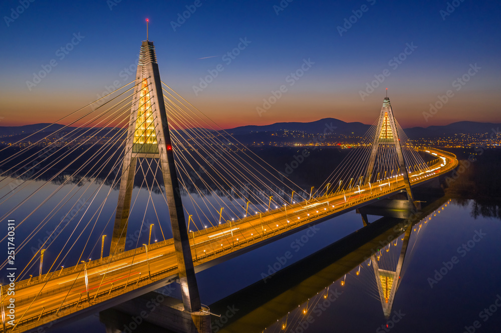 Fototapeta premium Budapest, Hungary - Aerial view of the illuminated Megyeri Bridge at dusk with clear blue sky