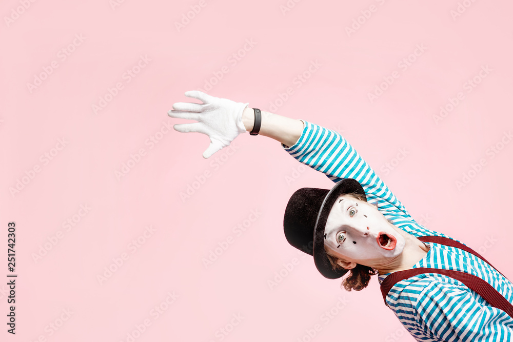 Emotional pantomime with white facial makeup showing empty space of the pink background, advertising something - obrazy, fototapety, plakaty 