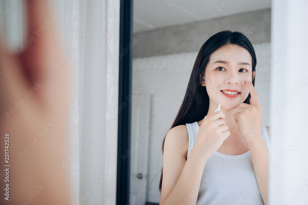 Beauty Asian Woman use Acne Gel Skincare after Cleansing on Face His Happiness and Look at mirror in White Bedroom. Beauty Asian Woman use Acne Gel Skincare after Cleansing on Face His Happiness and Look at mirror in White Bedroom.
