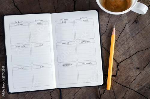 Top view of open page diary with yellow pencil and cup of coffee on wooden background. photo