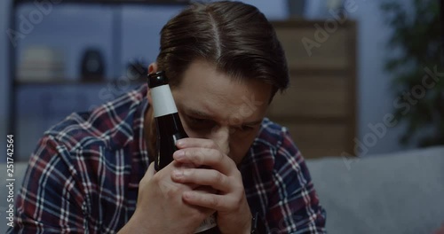 Close up of the sad depressed man sitting with a bottle of beer on the sofa in the dark room and being in stressed state of mind. photo