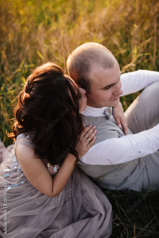 Wedding near the river in field at sunset with brown horse. Bride in light airy dress in color of dusty rose. Beige dress with sparkles. Light suit with bow tie. bride and groom embrace and kiss. Wedding near the river in field at sunset with brown horse. Bride in light airy dress in color of dusty rose. Beige dress with sparkles. Light suit with bow tie. bride and groom embrace and kiss.