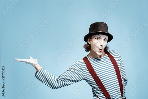 Emotional pantomime with white facial makeup showing empty space on the blue background, advertising something