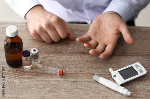 Diabetic man with lancet pen, digital glucometer and medicines at table, closeup