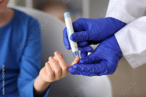 Doctor taking blood sample of diabetic child in clinic