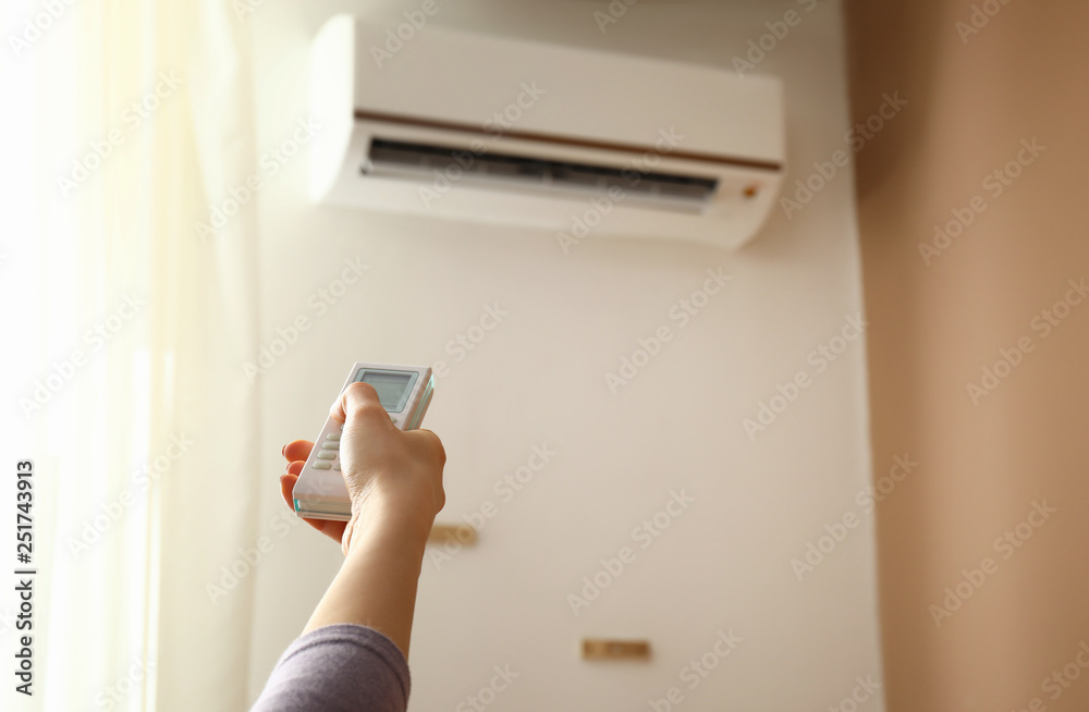 Young woman switching on air conditioner at home Young woman switching on air conditioner at home