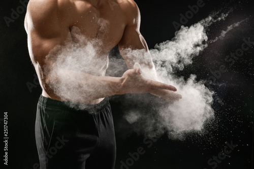 Young sporty man applying talc on hands against dark background