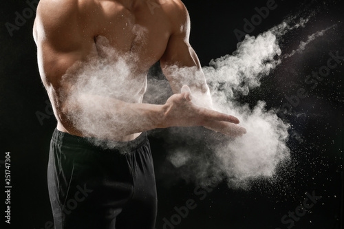 Fotografía Young sporty man applying talc on hands against dark background