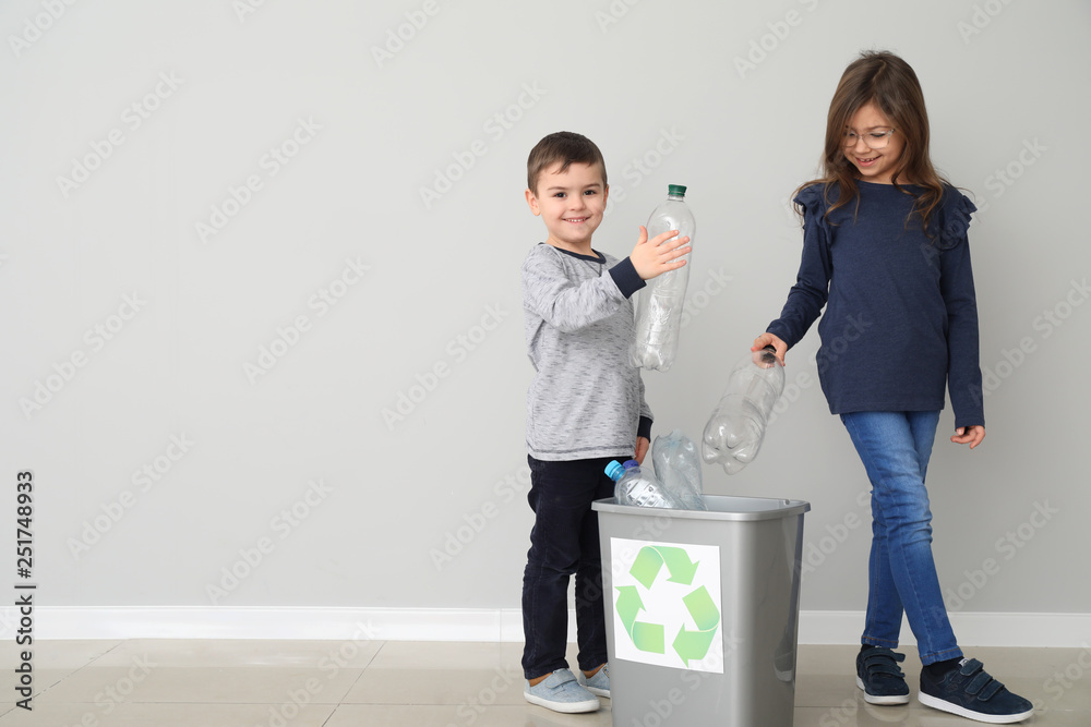 Children throwing garbage into trash bin near light wall. Recycling