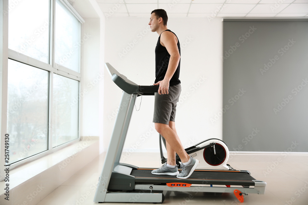Fototapeta premium Sporty young man on treadmill in gym