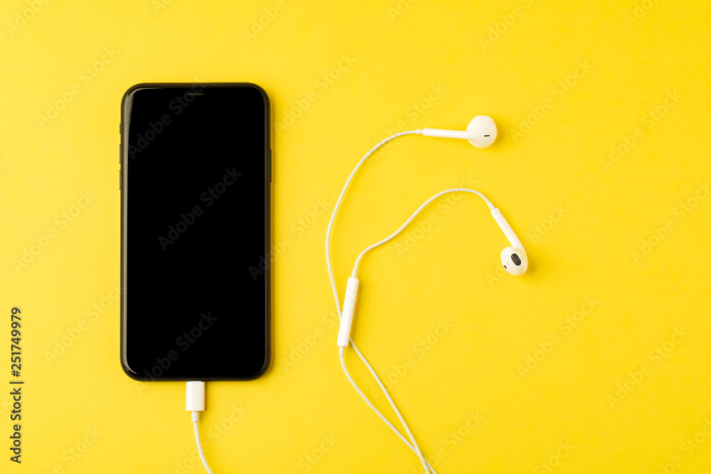 Smartphone with headphones on yellow background. The view from the top. Listen to music. Smartphone with headphones on yellow background. The view from the top. Listen to music.