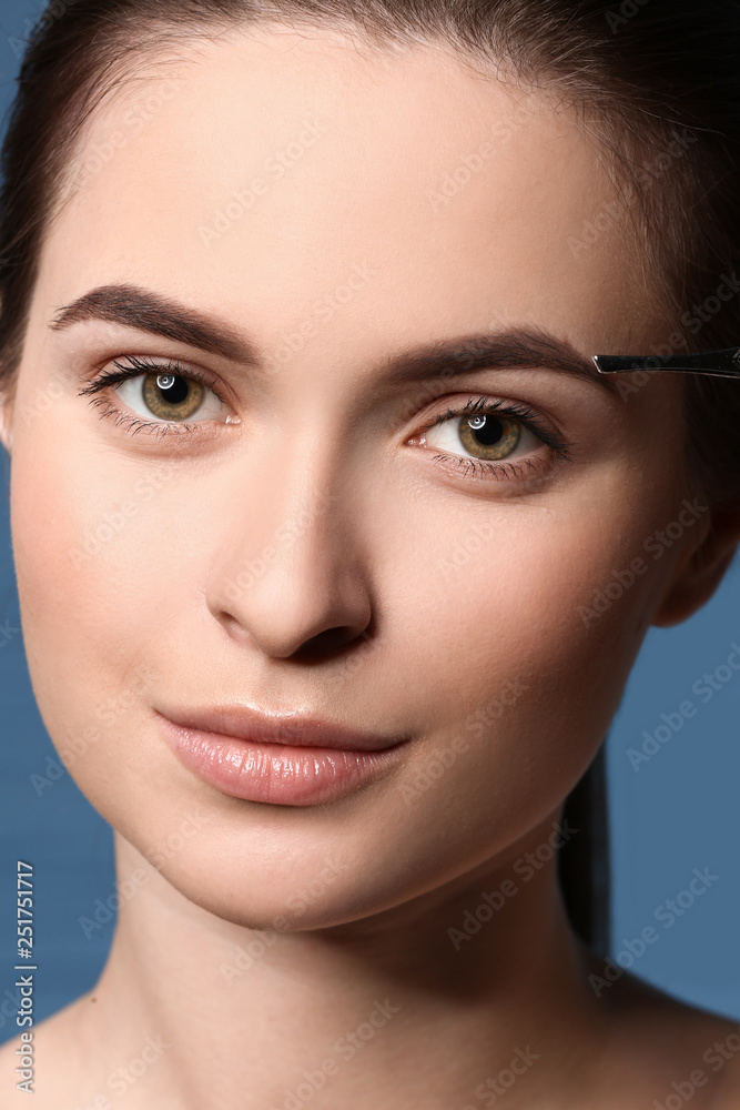 Young woman undergoing eyebrow correction procedure on color background, closeup