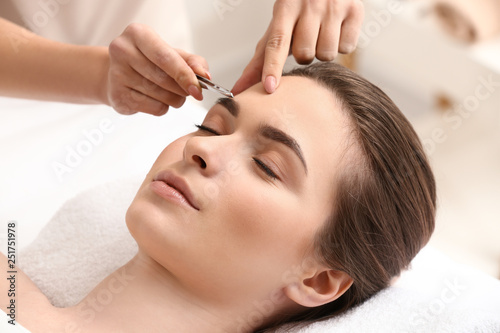 Canvas Print Young woman undergoing eyebrow correction procedure in beauty salon