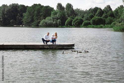 young family feeds wild ducks sitting on a pier by the lake