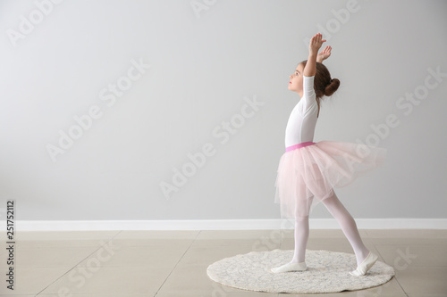 Cute little ballerina dancing near light wall