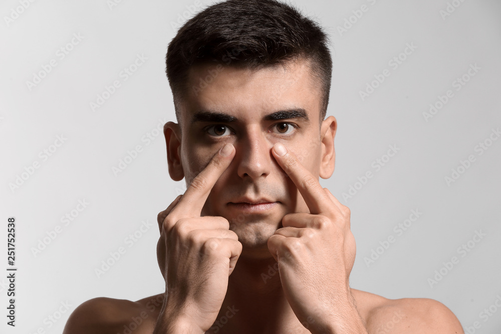 Man giving himself face massage on light background Man giving himself face massage on light background