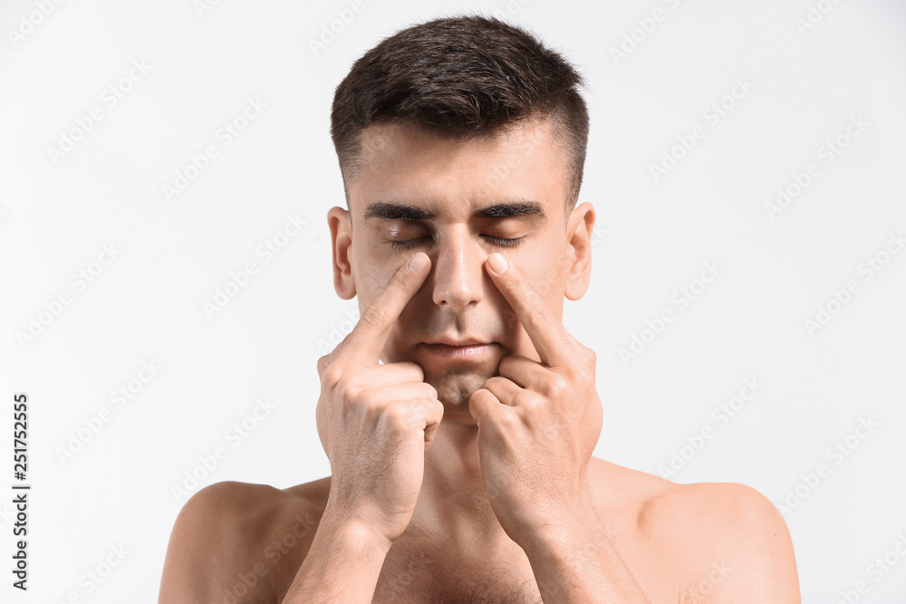 Naklejka premium Man giving himself face massage on light background