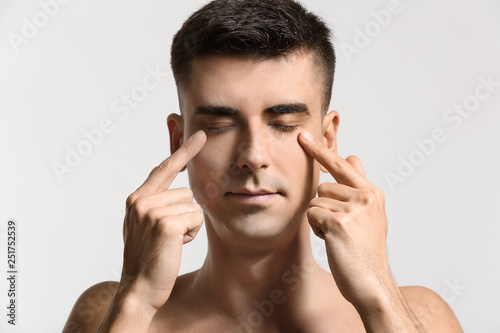 Man giving himself face massage on light background