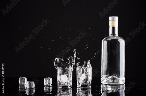 bottle of vodka with glasses and splashes on a black background photo