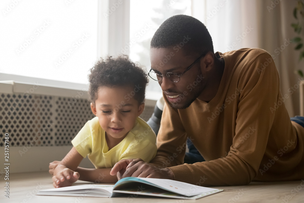 Happy black father and toddler son reading book at home Happy black father and toddler son reading book at home