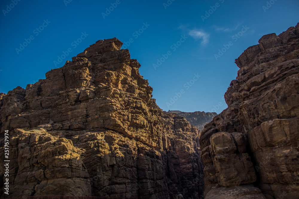 steep desert bare mountain rocks in canyon environment foreshortening from below on blue sky background 