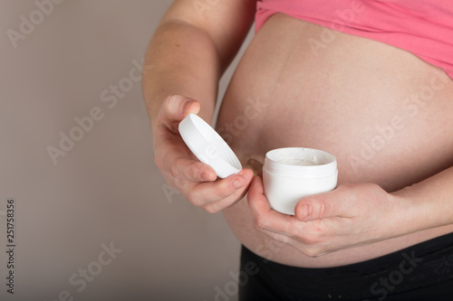 Young pregnant woman keeps skin cream care close to her belly.