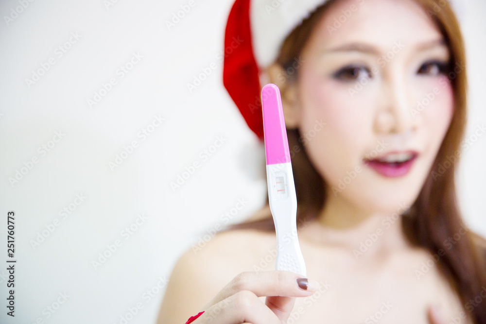 Young attractive girl wear santa suit and santa hat hold a pregnancy test and standing on white background. christmas festival. image for background and copy space. baby is gift from god concept. Young attractive girl wear santa suit and santa hat hold a pregnancy test and standing on white background. christmas festival. image for background and copy space. baby is gift from god concept.