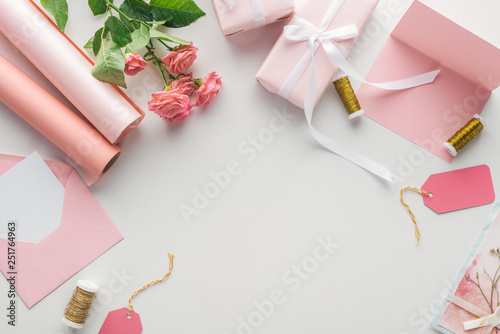 top view of pink roses, rolls of paper, wrapped gifts, envelope and greeting card on grey background