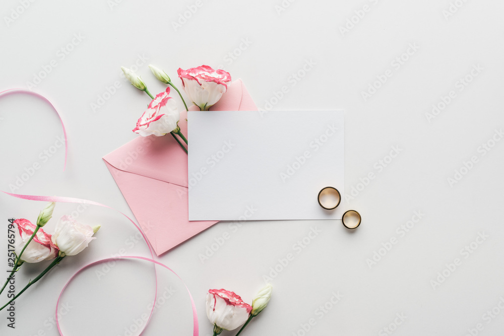 top view of empty card with pink envelope, flowers, silk ribbon and golden wedding rings on grey background top view of empty card with pink envelope, flowers, silk ribbon and golden wedding rings on grey background