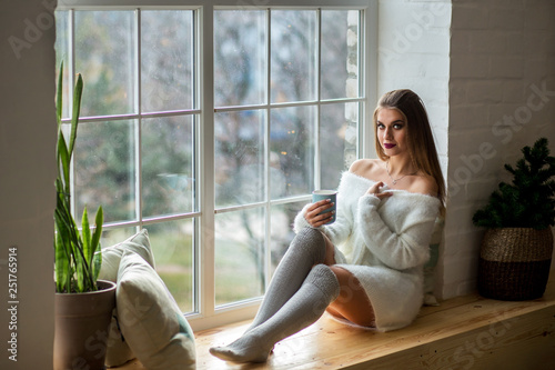 beautiful girl sitting on the windowsill near the window with a cup of tea