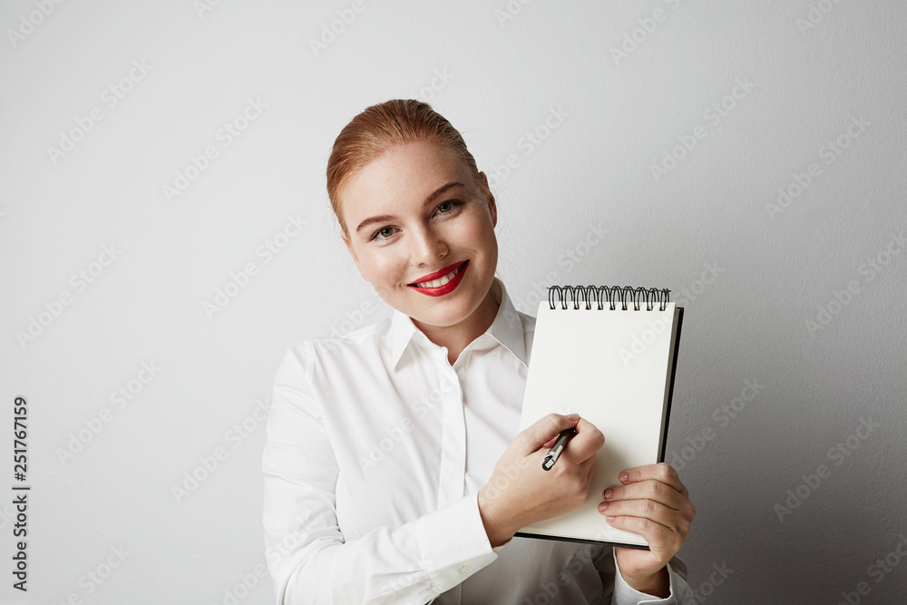 Portrait of trendy redhead woman posing in shirt holding empty notepad over white background Portrait of trendy redhead woman posing in shirt holding empty notepad over white background