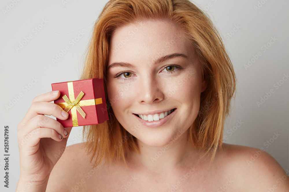 Beauty redhead woman holding hand red gift box over white empty background Beauty redhead woman holding hand red gift box over white empty background