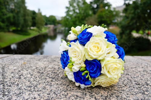Wedding bouquet from blue and white roses in city park on stone texture and river background