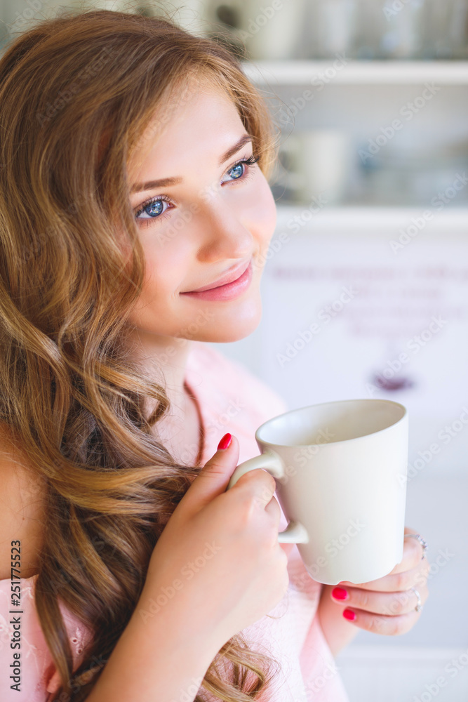 The young smiling girl early in the morning in kitchen drinks water from a mug The young smiling girl early in the morning in kitchen drinks water from a mug