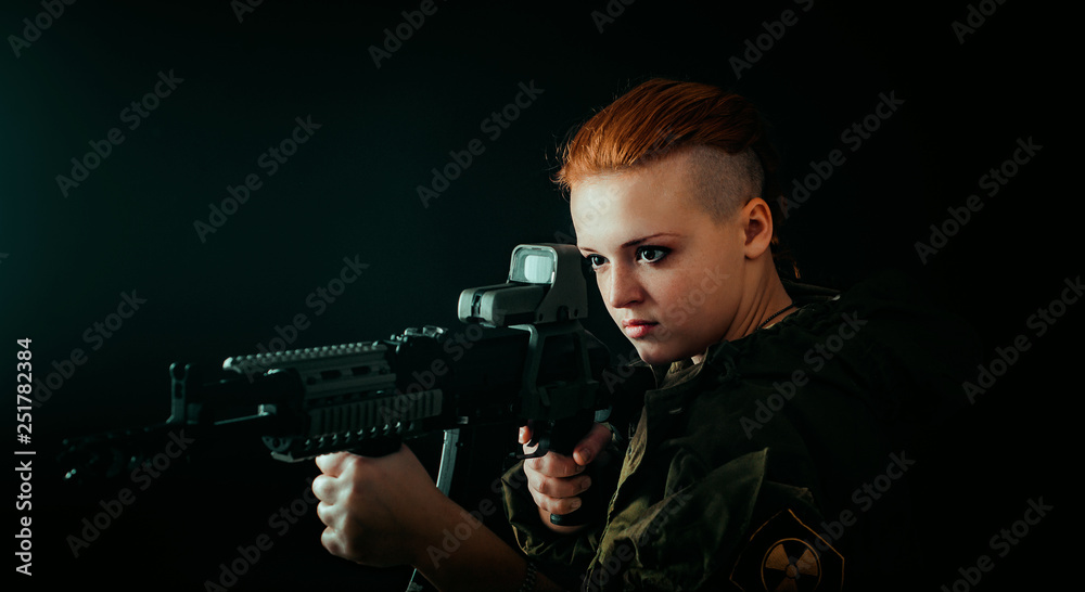 Young woman with red hair, hold machinegun and takes aim at the sight in military uniform. horizontal background