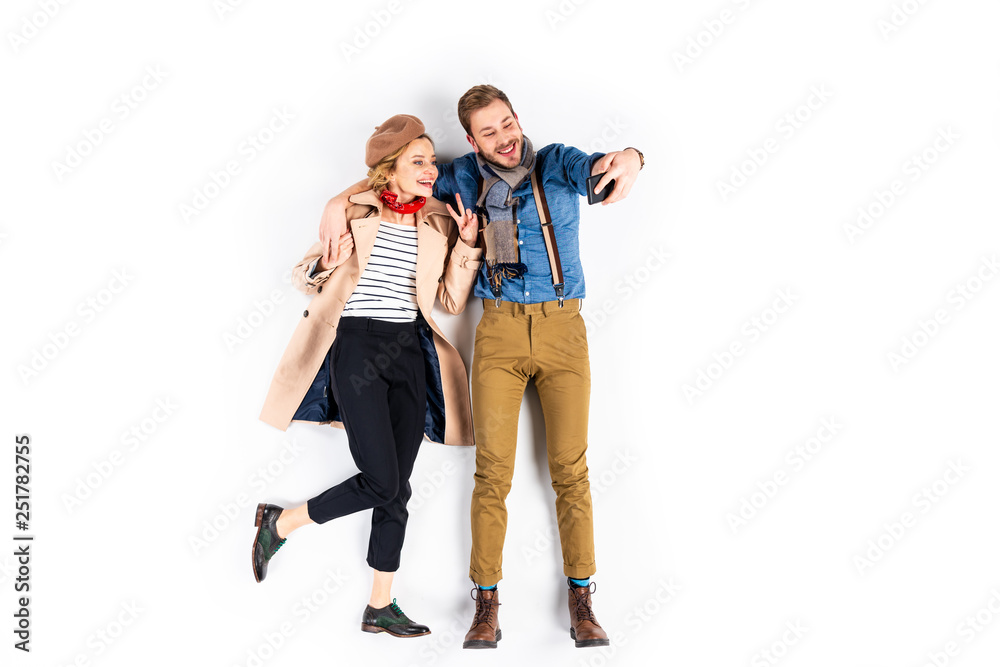 Fototapeta premium Stylish woman showing peace sign while taking selfie with boyfriend on white background
