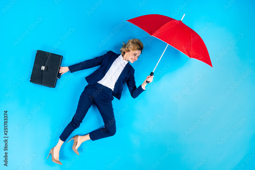 Woman with briefcase posing with red umbrella on blue background - obrazy, fototapety, plakaty 