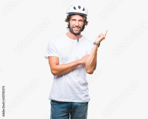 Handsome hispanic cyclist man wearing safety helmet over isolated background with a big smile on face, pointing with hand and finger to the side looking at the camera.