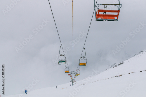 Empty old lifts for two people. Dvuhkreselny ski lift in the snow and fog. Multicolored broken gondolas in Dombai, Caucasus, Karachay-Cherkessia, Russia.